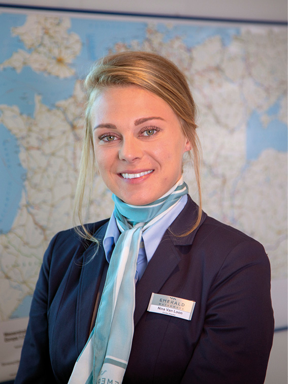 Woman smiling, wearing smart clothing in her office, with a map on the white wall behind her