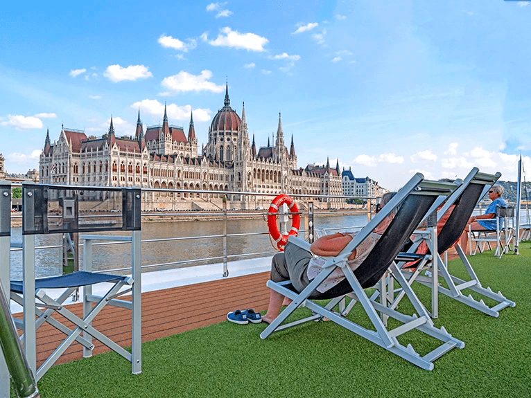 Guests on the sun deck of a Scenic cruise ship in Budapest, looking at the Hungarian Parliament Building.