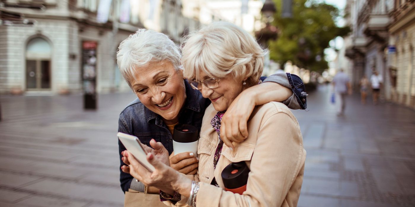 Close up of two female senior friends using a phone while having a walk in the city"