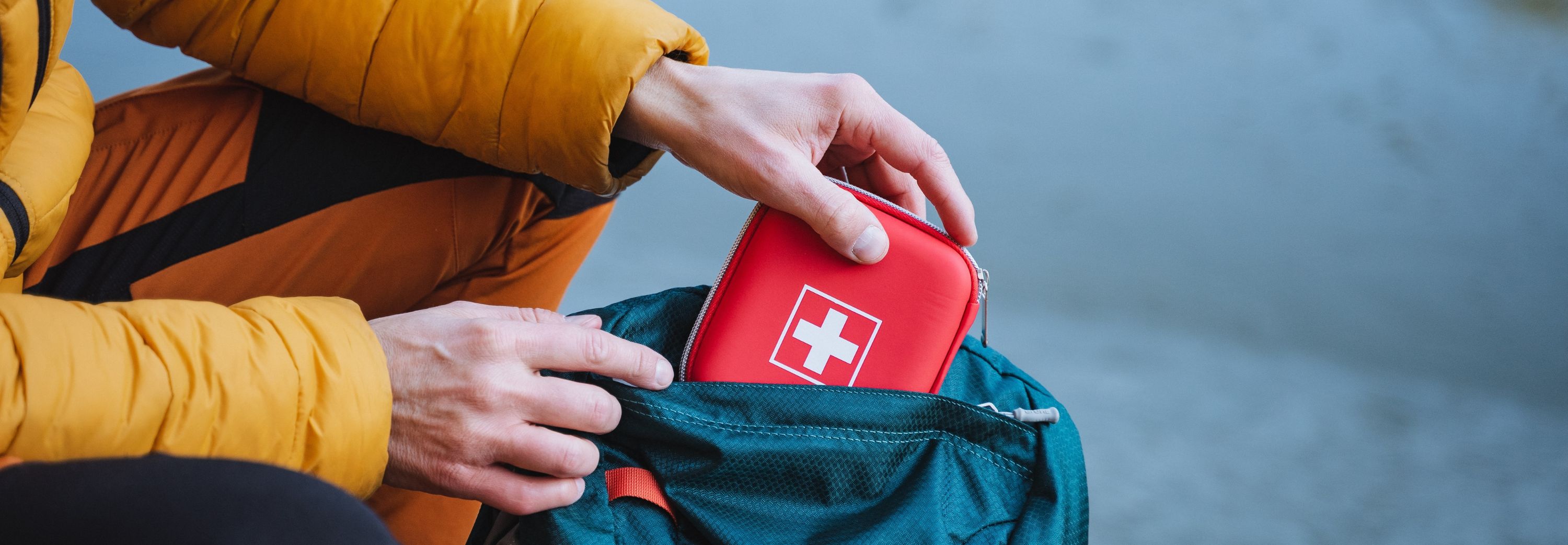 A guy puts a first aid kit in a backpack, packing things for a hike
