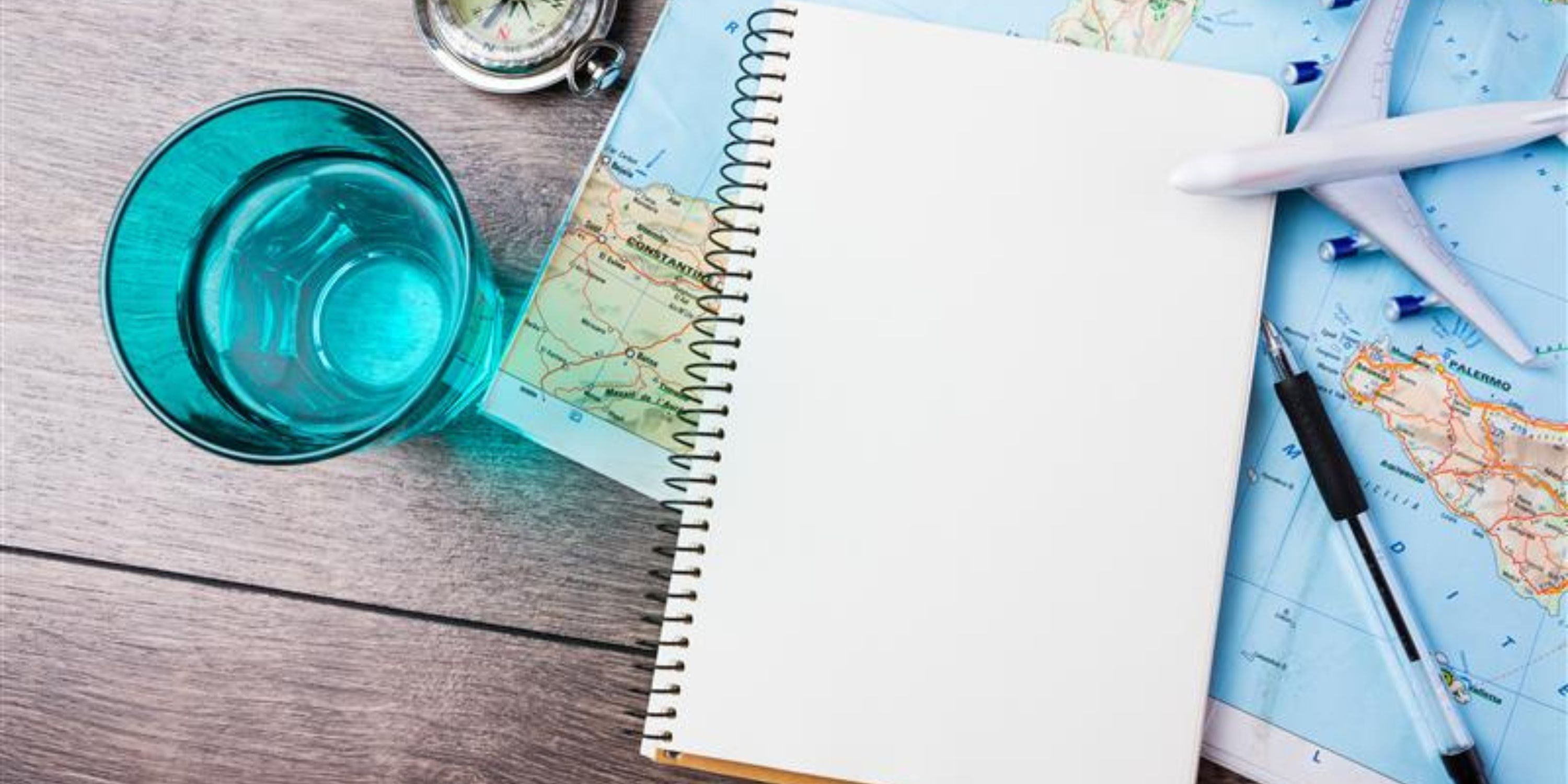 Close up of compass, glass of water note pad, pen and toy airplane and touristic map on wooden table