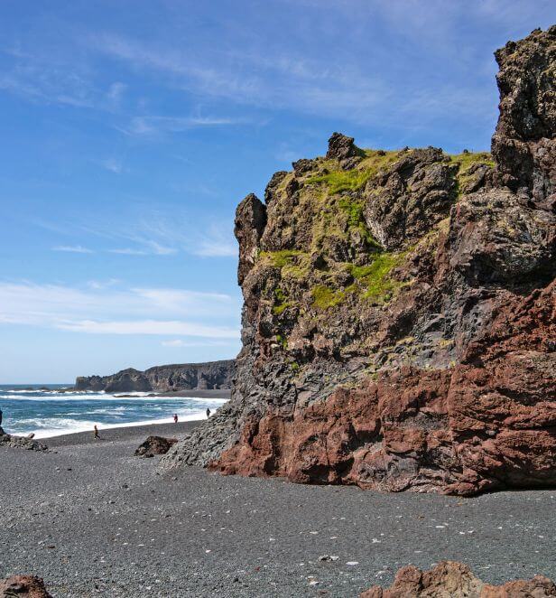 Volcanic cliffside with patches of green moss rising from a black sand beach in Grundarfjörður, Iceland