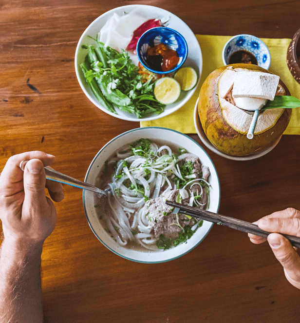 Traditional bowl of Vietnamese pho with beef slices, rice noodles, fresh herbs, and lime on the side.