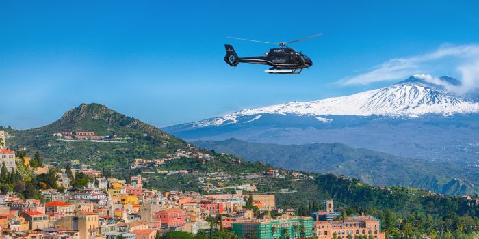 Scenic Eclipse helicopter flying over colorful Italian hillside town with Mount Etna in the background