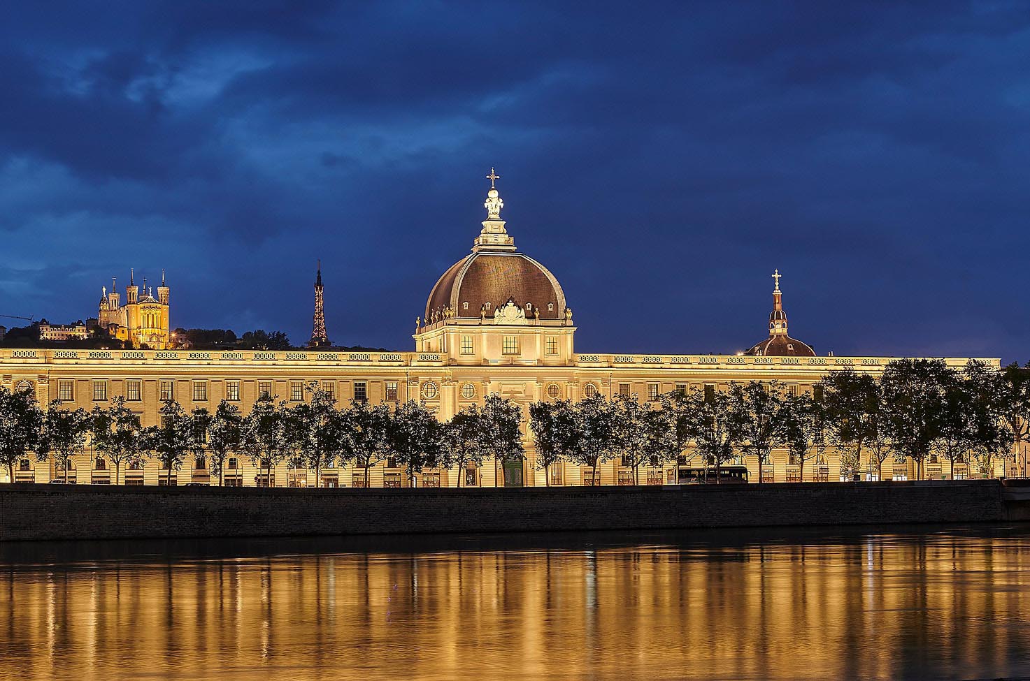 The Intercontinental Lyon hotel exterior illuminated at night with the lights reflecting in the Rhone river. 